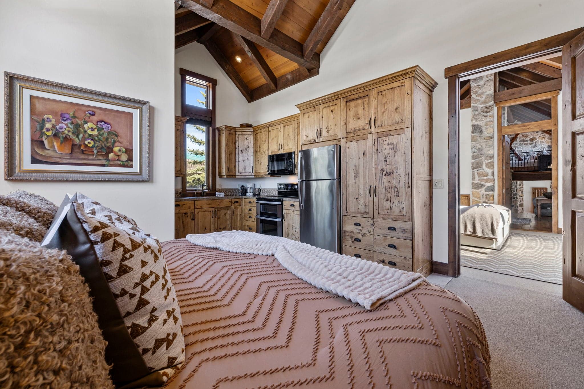 Guest suite with patterned bedding, vaulted ceiling, and rustic wood cabinetry.