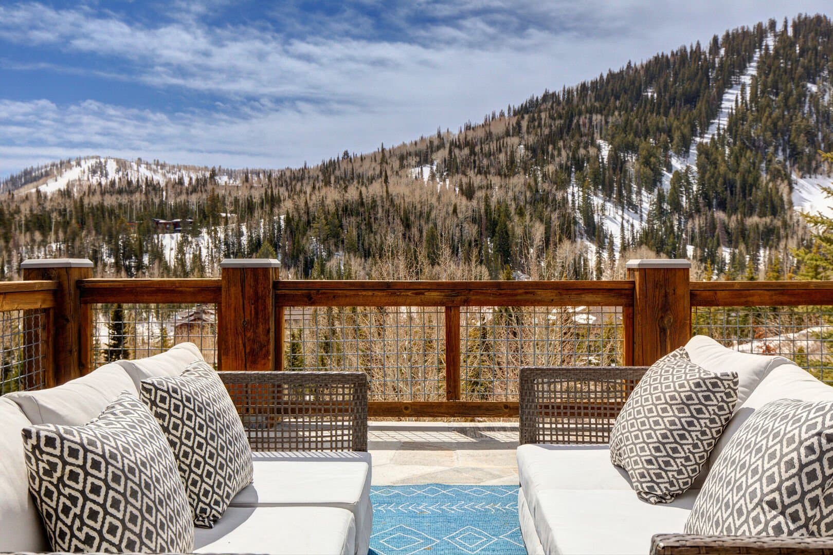 Two outdoor couches face each other on the patio of this luxury Park City vacation rental, overlooking snowy mountain trees.