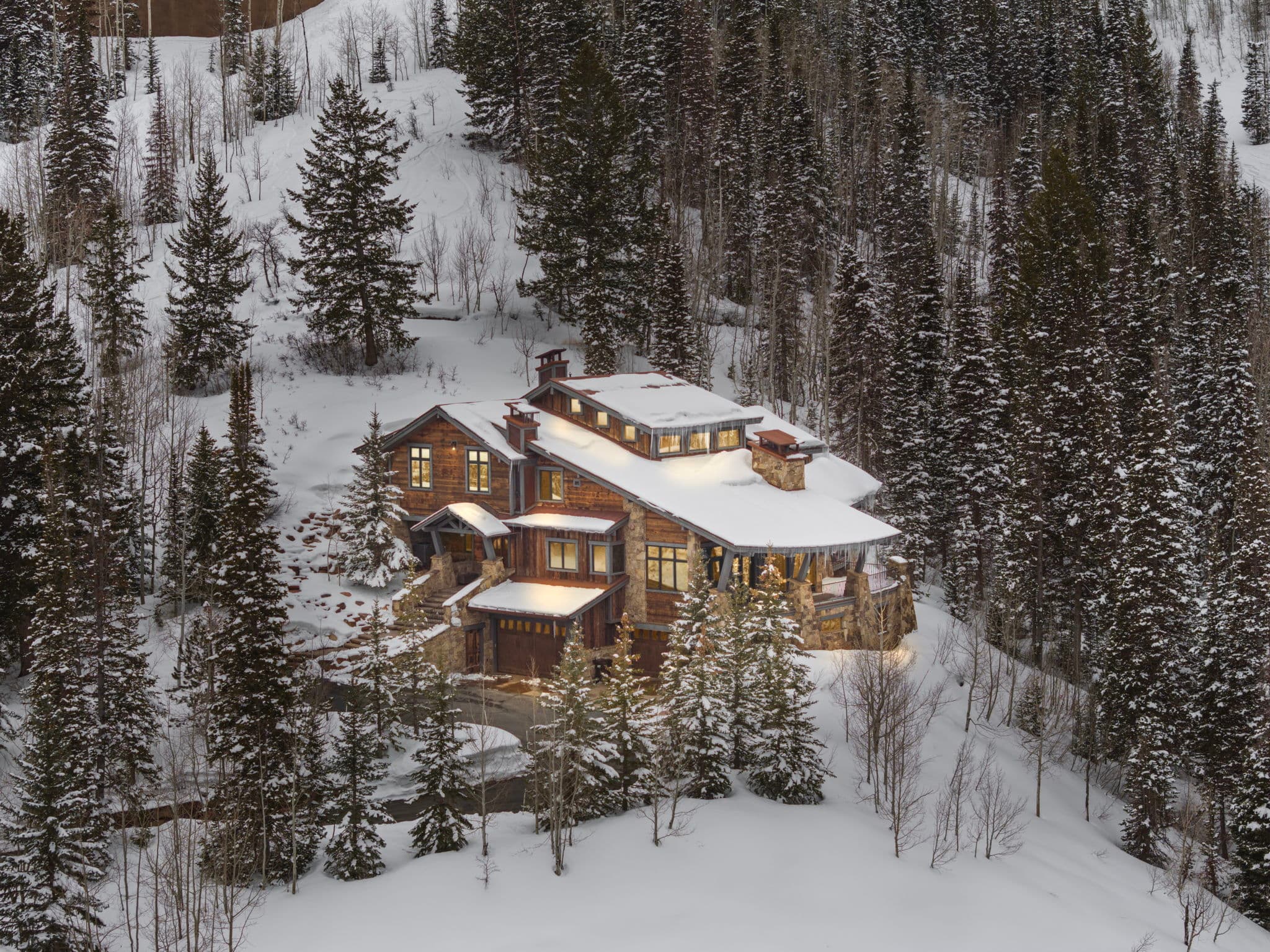 a view of Silver Horse in Park City from far away. you can see the ski slopes around the home and the mountain terrain. the home has snow on the roof and snow covers the forested terrain around it.