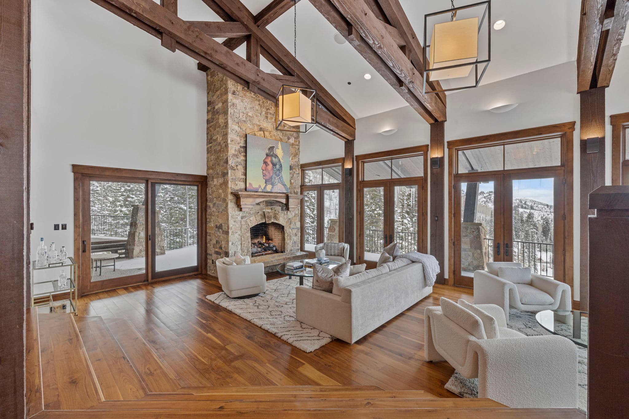 a view of the living room with tall ceilings and wood beams and a large stone fireplace. there are views of the mountains outside the windows