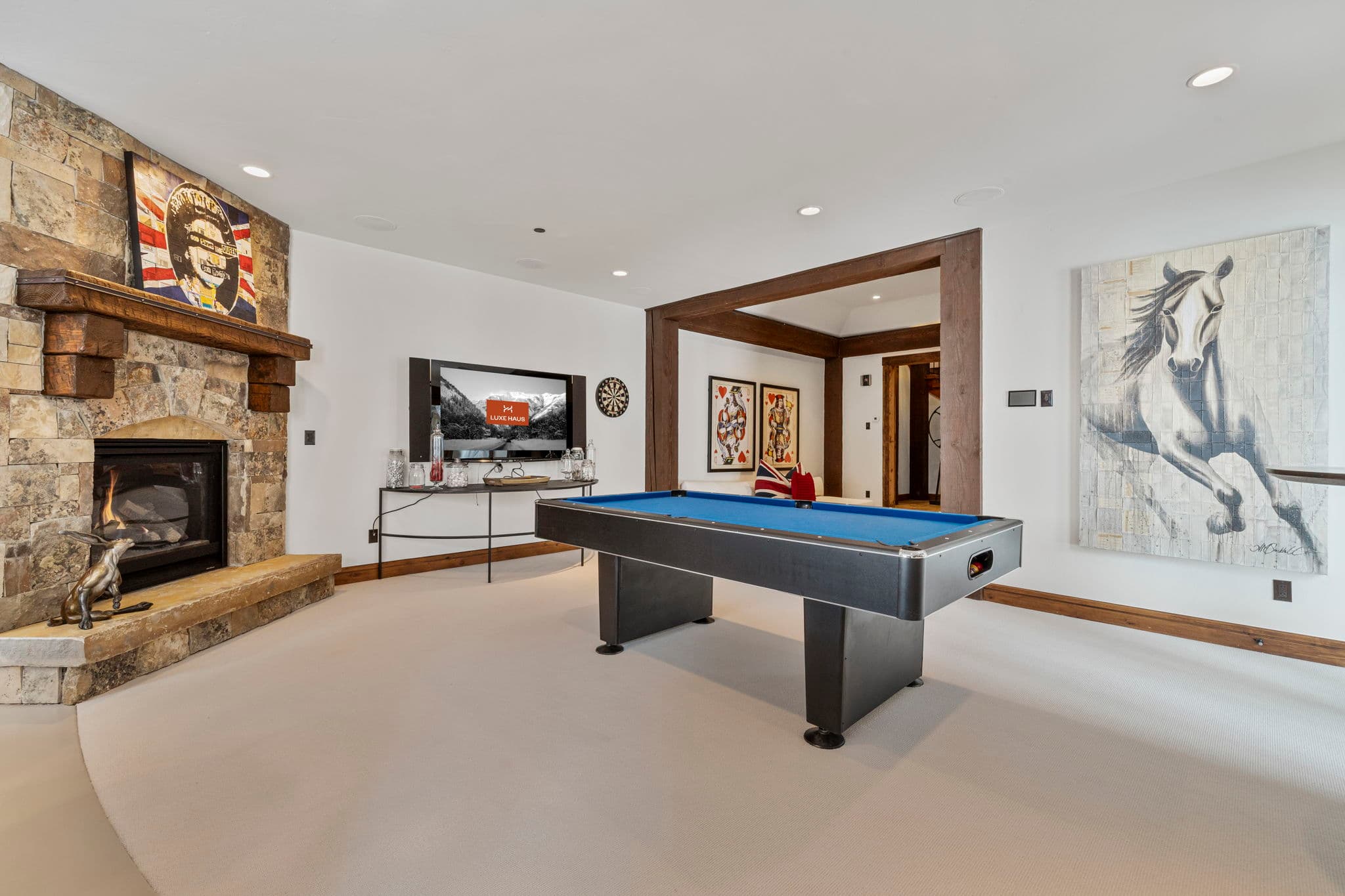 a large stone fireplace in the game room with TV and pool table. The TV has Luxe Haus displayed on the screen